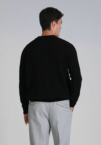 Pull en maille noir avec un col rond et un motif à côtes verticales, associé à un pantalon taillé gris clair.