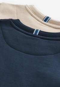 Due maglioni a collo rotondo: uno blu navy e uno beige. Entrambi presentano colli a coste con accenti striati blu e bianchi. Tessuto morbido e testurizzato.