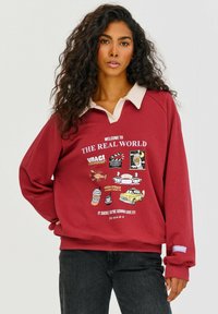 Bordová mikina s límcem v světle béžové barvě, na přední straně s barevnými grafikami a textem. Dlouhé rukávy s manžetami.