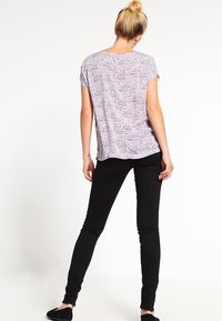 Lila mönstrad kortärmad topp med en lös passform, kombinerad med svarta tajta jeans. Toppen har en subtil geometrisk design och en mjuk textur.