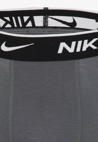 Graue Sportunterwäsche mit einem schwarzen, elastischen Bund, auf dem das "NIKE"-Logo in Weiß zu sehen ist. Glatte Textur mit verstärkten Nähten.