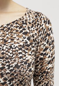 Top w leopardzim wzorze z okrągłym dekoltem i krótkimi rękawami, wykonany z miękkiego materiału w odcieniach beżu, brązu i czerni.