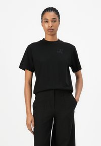 Svart kortärmad t-shirt med rund halsringning och subtilt präglad logotyp på bröstet, gjord av mjukt bomullstyg, i kombination med svarta skräddarsydda byxor.