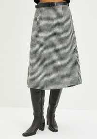 Falda en línea A hasta la rodilla en un patrón de jaquard blanco y negro, hecha de tela texturizada, combinada con botas de cuero negro hasta la rodilla.