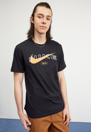 T-shirt in cotone nero con un grande logo Nike arancione e accenti bianchi e l'anno 1972, maniche corte e vestibilità comoda.