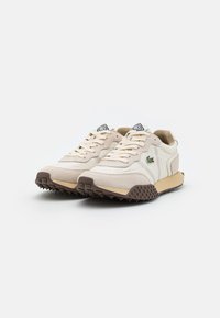 Beige spordijalatsid, millel on sileda ja nubukiteksti segu, pruuni kummitald, mis pakub haakuvust, ja logode detail keelega.