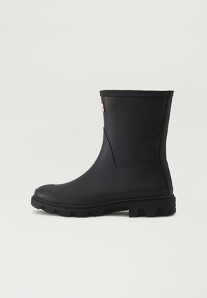 Zwarte rubberen regenlaars met een ronde neus, lage hak en een gestructureerde zool. Heeft een gladde afwerking en een klein rood logo aan de zijkant.