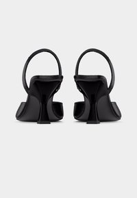 Μαύρα γυναικεία παπούτσια με ψηλό τακούνι και ιμάντες slingback με υφή, εμφανιζόμενα από πίσω σε απλό ανοιχτό γκρι φόντο.