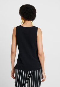 Czarny top bez rękawów o prążkowanej fakturze, z okrągłym dekoltem i luźnym krojem. Nosi się go z czarno-białymi spodniami w paski.
