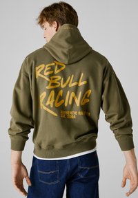 Hoodie vert olive avec poche kangourou à l'avant, poignets côtelés et grand texte doré "RED BULL RACING" au dos. Tissu doux et texturé.