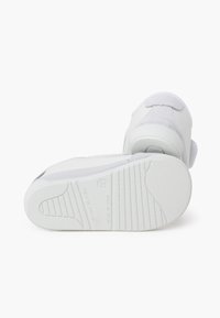 Bílé tenisky kombinující hladké a semišové textury, pevnou gumovou podrážku s vzorkem a minimalistické designové detaily.