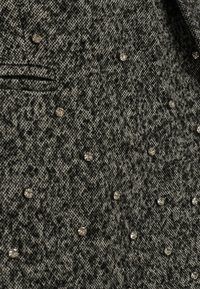 Tessuto grigio strutturato con embellishments argentati sparsi e un motivo sottile. Include una piccola tasca con flap.