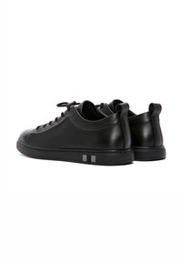 Sneaker in pelle nera con punta rotonda, lacci piatti e suola in gomma testurizzata. Presenta un sottile accento grigio nell'area del tallone.