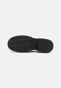 Zwarte rubberen zool met een gestructureerd patroon, voorzien van een reliëflogo. Effen kleur ontwerp met duidelijke profiel voor grip en duurzaamheid.