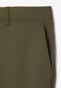 Pantaloni casual verde oliva con una finitura liscia e testurizzata, passanti per cintura e tasche laterali inclinate. Dettagli di cucitura minimali visibili.