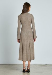 Abito lavorato a maglia in beige con texture a costine, maniche svasate e lunghezza intermedia. Presenta un corpetto aderente con una silhouette svasata.