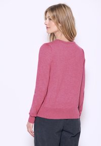 Rosa gestrickter Pullover mit rundem Halsausschnitt, langen Ärmeln und subtilen Puffdetails an den Schultern. Die Textur wirkt weich und leicht.