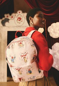 Ružový batoh s ilustráciami rozprávkových zvierat, červenými akcentmi, zipsovým uzáverom a polstrovanými popruhmi, ktorý vystavuje hravý dizajn a rôzne vzory.