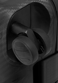 Primo piano di una ruota a doppia rotazione nera attaccata all'angolo di una valigia rigida con texture.