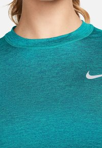 Turquoise athletic shirt made of breathable fabric. Features a crew neckline, short sleeves, and a small white Nike logo on the chest.