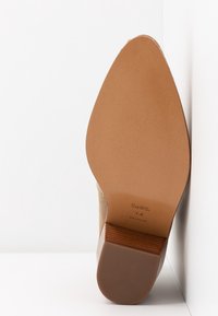 Podeszwa beżowego zamszowego buta na obcasie, rozmiar 7.5, z wytłoczonym logo Coach na skórzanej podeszwie i obcasie.