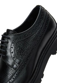 Zwarte leren dresschoenen met geperforeerde details, platte veters, een gestructureerd oppervlak en een stevige zool. Ronde teenontwerp met een subtiele glans.