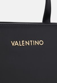 Svart läderhandväska med en guldfärgad "VALENTINO"-logotyp. Slät textur med rena linjer och minimalistisk design. Topphandtag för enkel bärning.