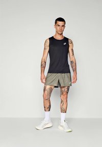 Svart trenings tank top med logo, olivengrønne shorts, hvite sokker og lyse sneakers; har tatoveringer på armer og ben.