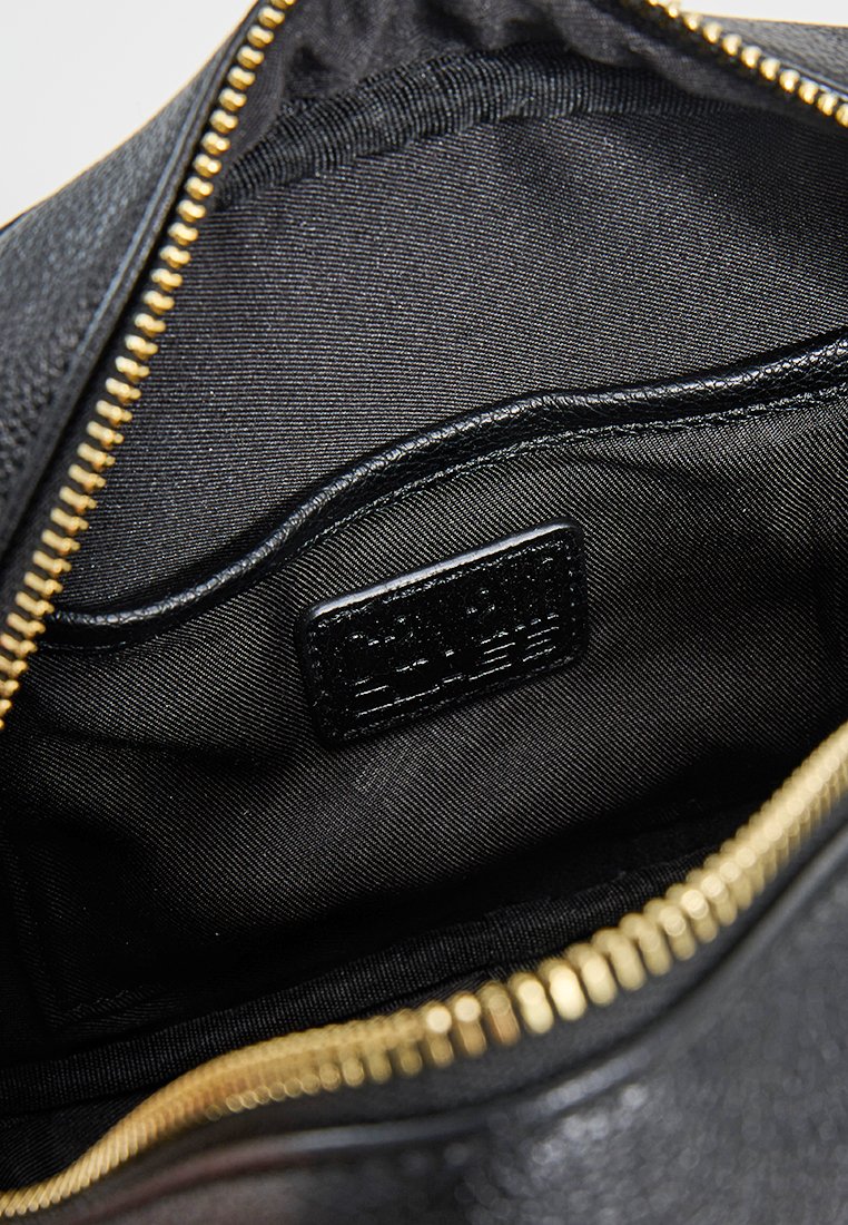 Intérieur d'un sac en cuir noir avec une texture lisse, équipé d'une fermeture éclair et d'une petite étiquette. Les accents dorés de la fermeture éclair contrastent avec le tissu.