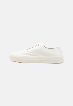 Baskets en toile blanches avec un bout rond, un laçage, des œillets dorés et une semelle en caoutchouc texturée. Style minimaliste, silhouette basse.
