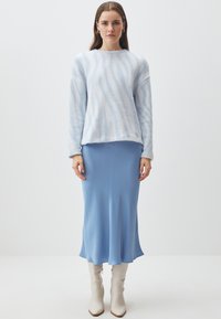 Maglione azzurro chiaro in peluche con strisce bianche texturizzate, abbinato a una gonna midi blu liscia e stivali bianchi lucidi fino al ginocchio.