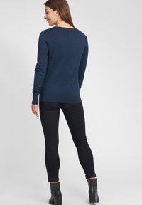 Marineblå langermet strikkegenser med rund hals, ensfarget tekstur og ribbede mansjetter, kombinert med svarte skinny jeans og ankelstøvler.