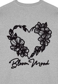 Felpa grigia con un design a cuore ricamato nero, fiori e il testo "Bloom Mood" in stile corsivo al centro.