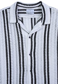 White and black striped short-sleeve shirt with a collared neckline. Textured, relaxed fit fabric with black buttons. Brand: Calliope.