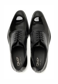 Scarpe eleganti in pelle nera con una finitura lucida, caratterizzate da un gambale testurizzato, design con lacci e una morbida fodera interna. Logo del marchio visibile all'interno.