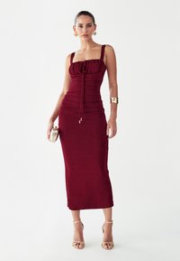 Vestido midi burdeos con tela fruncida, cordón ajustable en la parte delantera, escote cuadrado y tirantes finos. Textura suave, silueta ceñida.