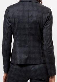 Blazer de cuadros negros hecho de tela suave. Presenta un cuello clásico y un diseño ajustado con patrones sutiles de cuadros.