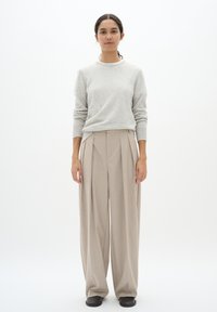 Maglione grigio chiaro in lana con maniche lunghe abbinato a pantaloni beige a pieghe, larghi. La modella indossa scarpe basse nere, presentata su uno sfondo bianco.