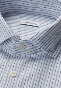 Chemise à rayures bleu clair et blanc avec des boutons blancs et une étiquette de marque "seidensticker" à l'intérieur du col.