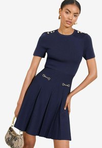 Dunkelblaues Kleid mit kurzen Ärmeln, tailliertem Oberteil, gefälteltem Rock, goldenen Hardware-Akzenten an Schultern und Taille sowie strukturiertem Stoff.