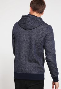 Felpa con cappuccio blu navy con tessuto strutturato, cappuccio con coulisse e polsini e orlo a coste, vista da dietro.