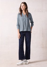 Blusa leggera blu a righe con scollatura a V e dettaglio dei bottoni abbinata a jeans a gamba larga blu navy scuro e sneaker bianche con accenti grigi.