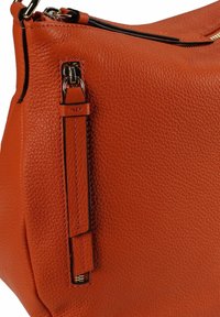 Oranje leren handtas met een gestructureerde afwerking, voorzien van een zijrits en een strak, schuin ontwerp voor gemakkelijke toegang. Geaccentueerd met glanzend beslag.