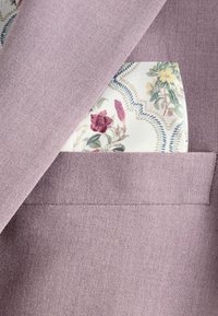 Il tessuto di un viola chiaro presenta un design strutturato, con un fazzoletto da taschino a motivo floreale visibile che spunta dalla tasca sul petto.