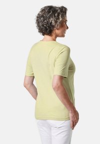 Grünes kurzärmeliges T-Shirt, runder Halsausschnitt, weicher Stoff, glatte Textur, taillierte Passform, getragen mit weißen Hosen.