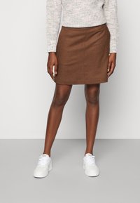 Bruine wollen rok met een rechte vorm, met een schone zoom. Gepaard met witte sneakers, gedragen met een lichtgestreept sweater.