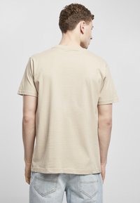 Beige bomull t-skjorte med korte ermer, rund halslinje og avslappet passform, vist fra ryggen mot en lys bakgrunn.