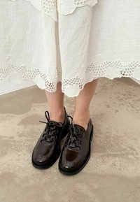 Scarpe stringate in pelle marrone con finitura lucida, punta rotonda e suola in gomma nera. Il design presenta sei fori per i lacci e lacci sottili.