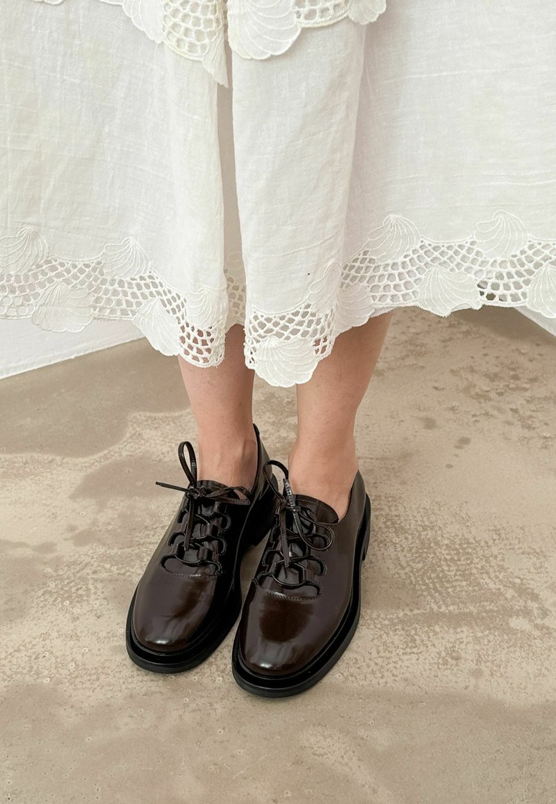 Scarpe stringate in pelle marrone con finitura lucida, punta rotonda e suola in gomma nera. Il design presenta sei fori per i lacci e lacci sottili.