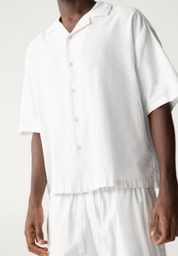 Wit linnen overhemd met korte mouwen en een reverskraag, met knopen aan de voorkant en een ontspannen pasvorm, gecombineerd met bijpassende lichte broek.